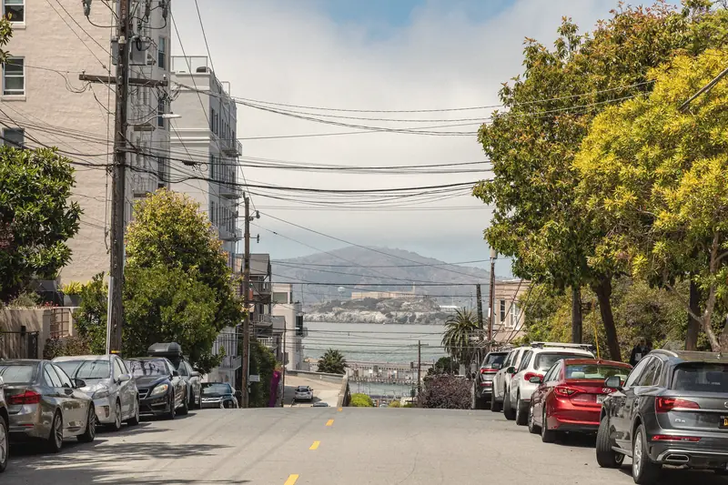 Photo of a residential street with parked cars sloping down toward the bay and Alcatraz